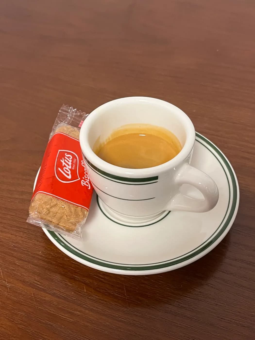 An espresso pulled on the La Pavoni, in a green-striped cup with a Lotus biscuit