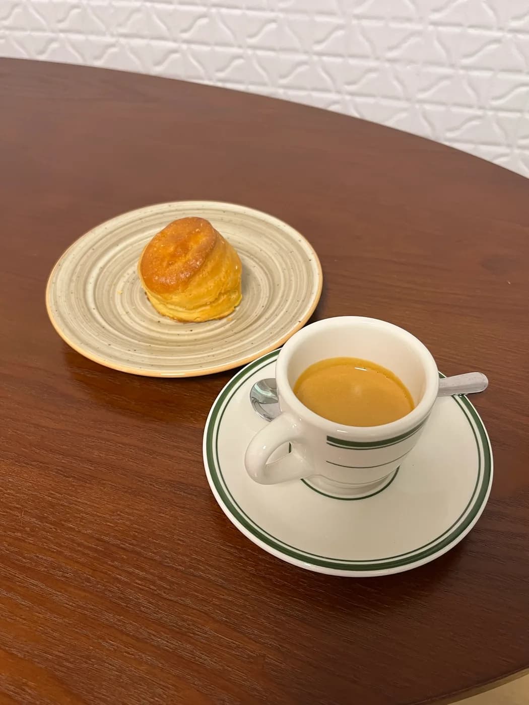 An espresso in a green-striped cup beside a small pastry
