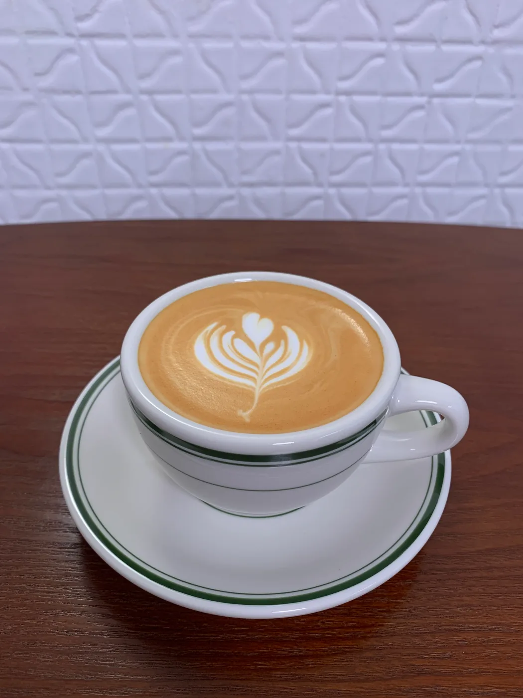 A flat white with a rosetta poured in a green-striped cup