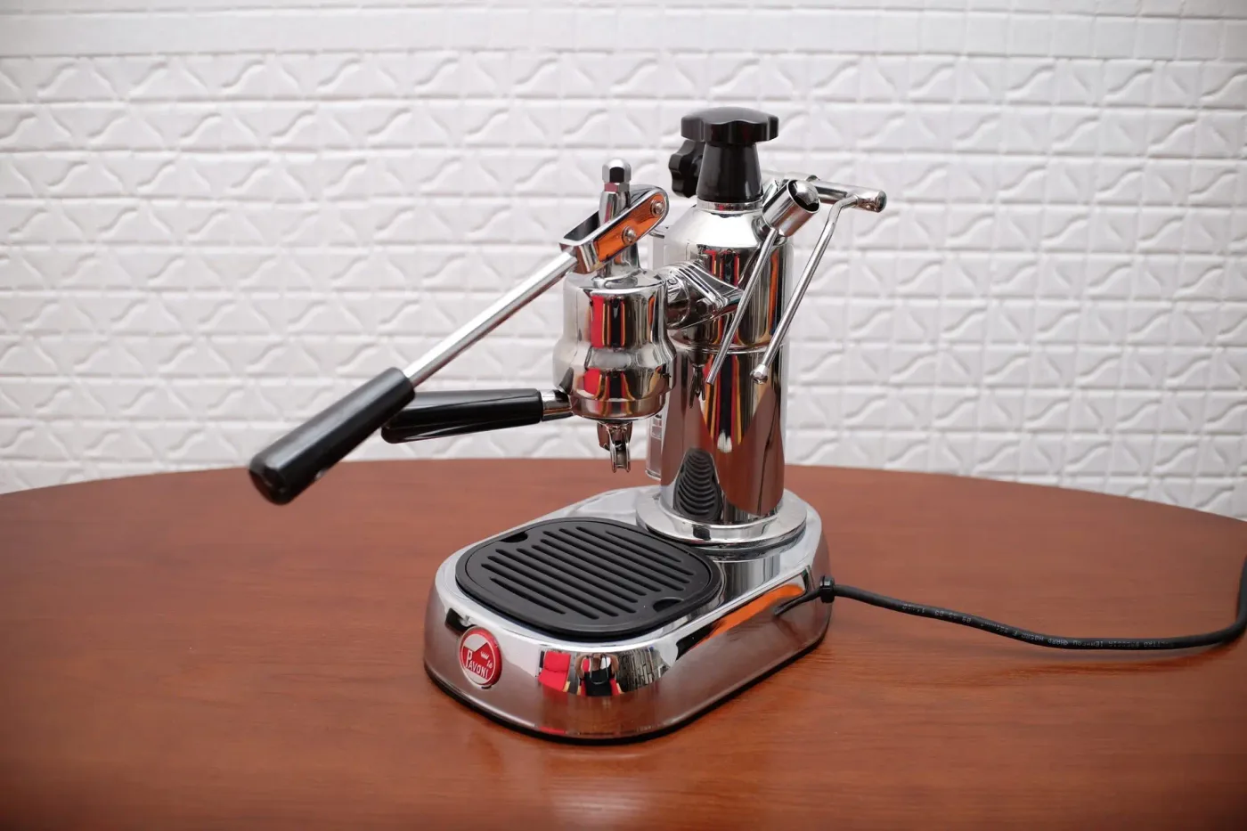 The La Pavoni lever espresso machine, chrome, against a white brick wall